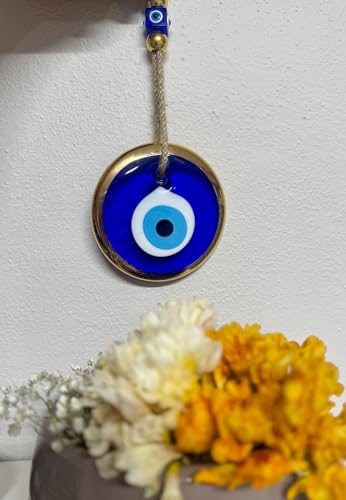 Evil eye pendant with a blue center and gold frame, hanging above flowers on a white background