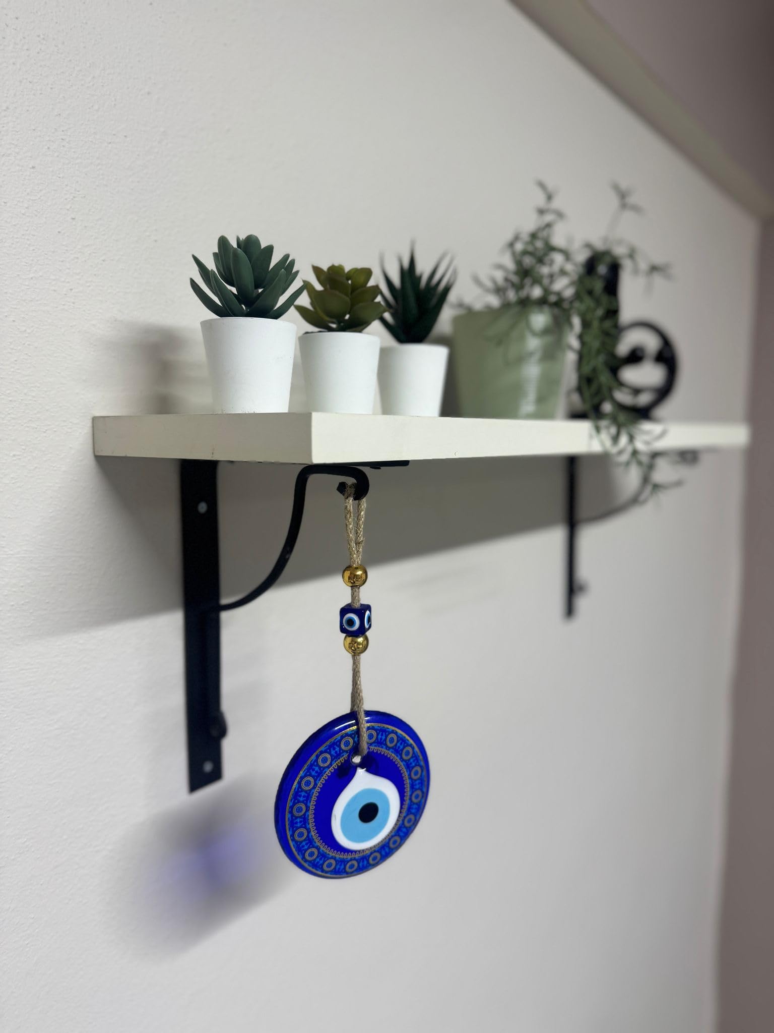Blue evil eye pendant hanging from a shelf with plants in the background