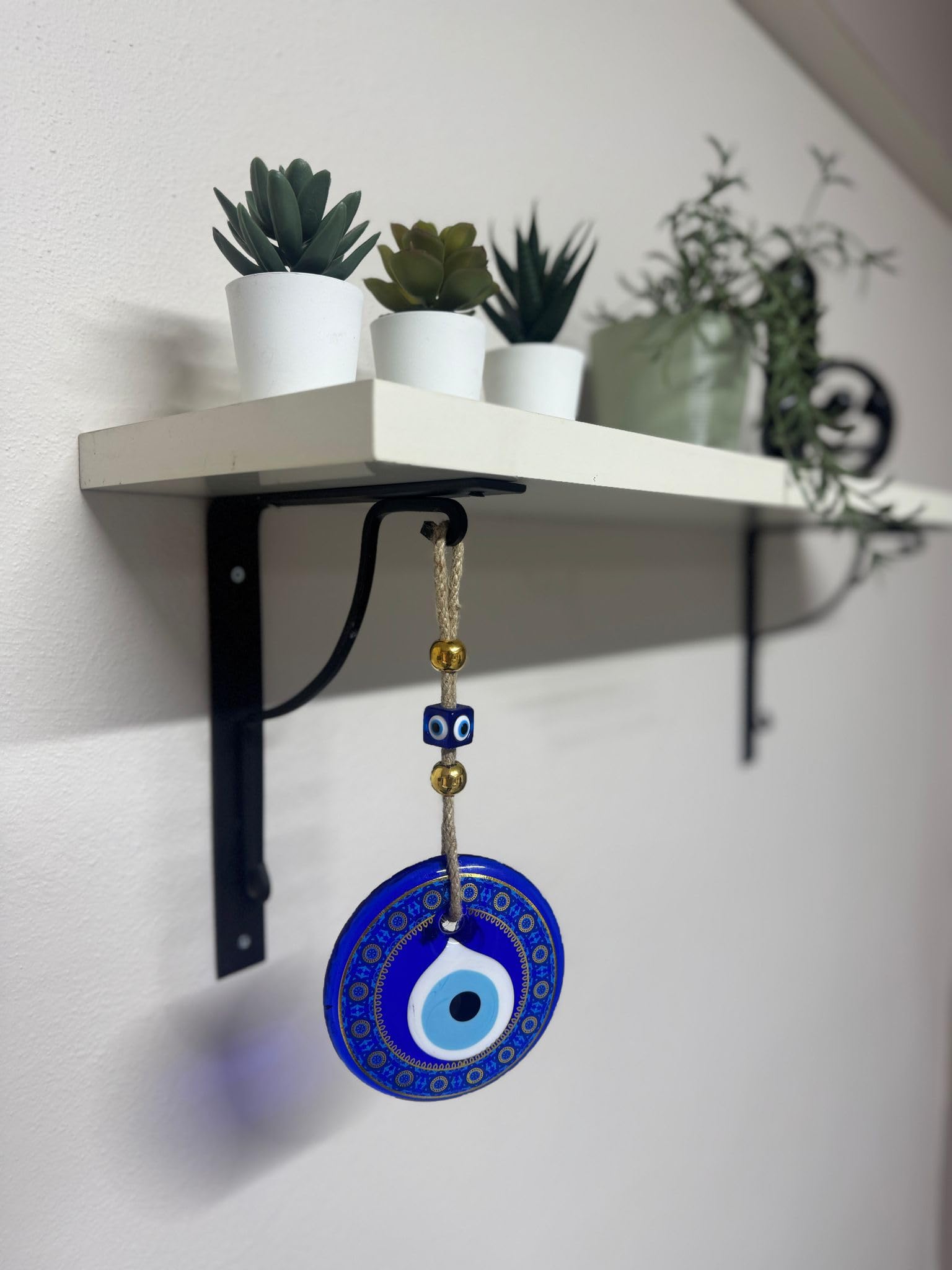 Decorative blue evil eye pendant hanging from a shelf with plants in the background.